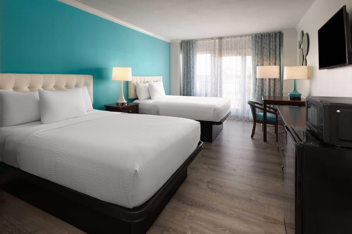 Une chambre d’hôtel avec deux lits, un bureau, une chaise, une télévision et un réfrigérateur.