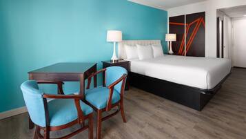 A hotel room with a bed, two bedside tables with lamps, a desk with two chairs, and a teal-colored wall.