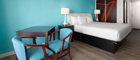 A hotel room with a bed, two bedside tables with lamps, a desk with two chairs, and a teal-colored wall.