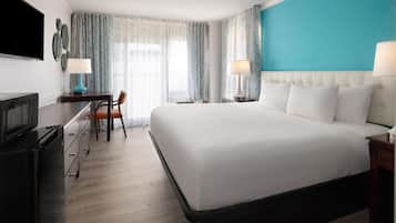 Quarto de hotel com uma cama grande, uma escrivaninha com cadeira, televisão e janela com cortinas.