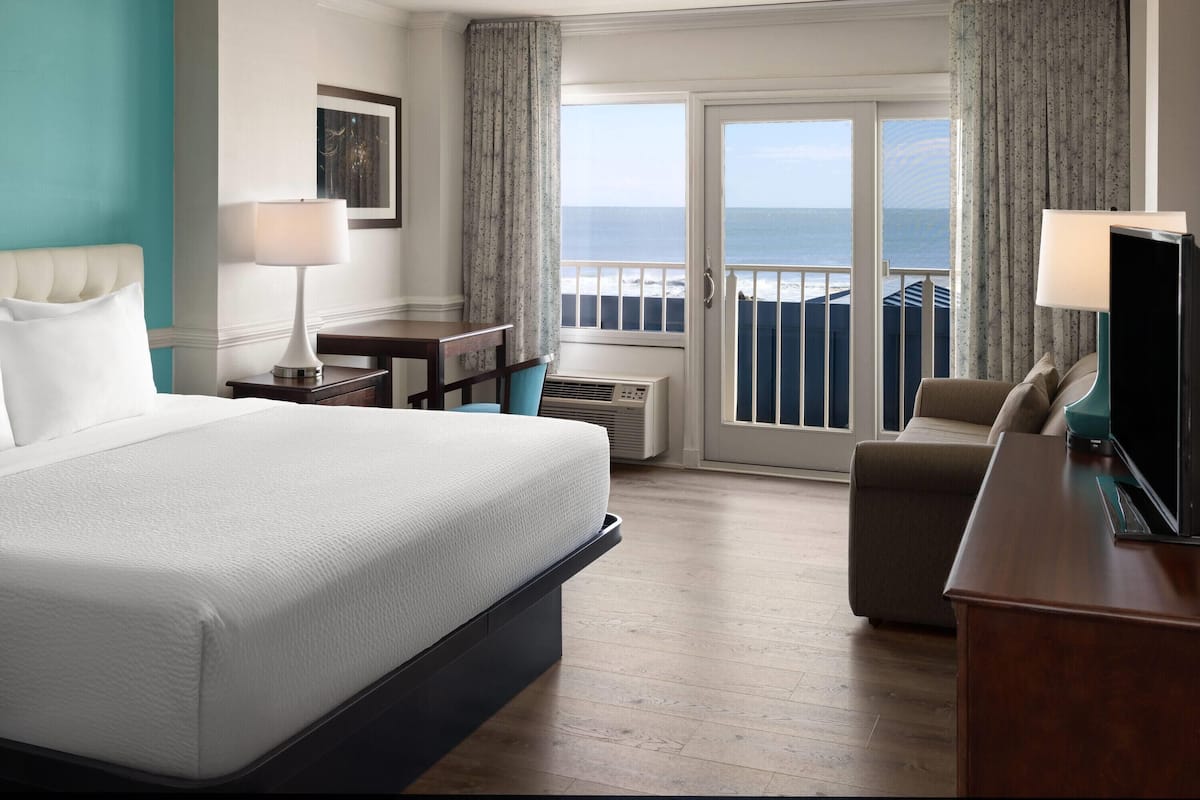 Une chambre d’hôtel équipée d’un lit, d’un bureau, d’une chaise, d’une télévision et offrant une vue sur l’océan grâce à une porte coulissante.