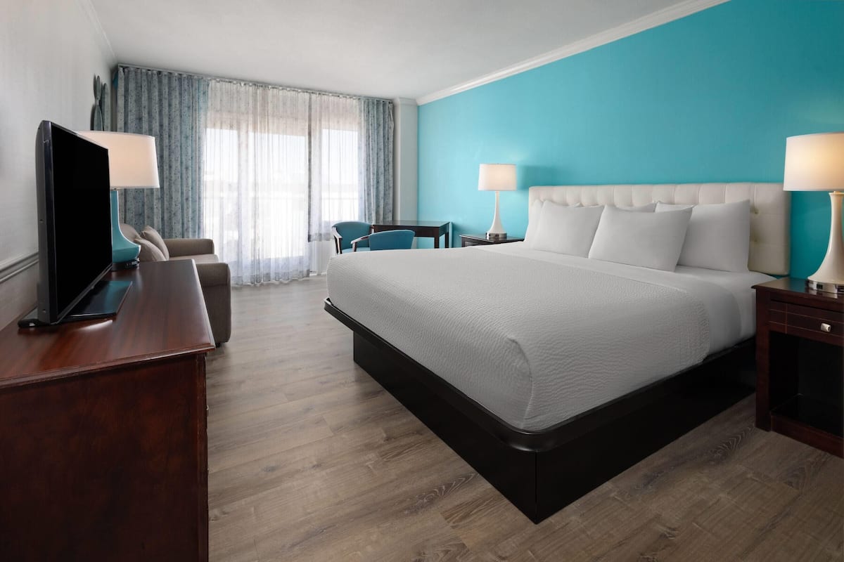 Une chambre d’hôtel avec un grand lit, un bureau avec une télévision, une chaise et une fenêtre avec des rideaux.