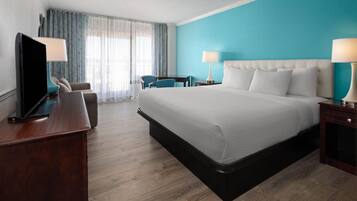 Habitación de hotel con una cama grande, un escritorio con televisor, una silla y una ventana con cortinas.