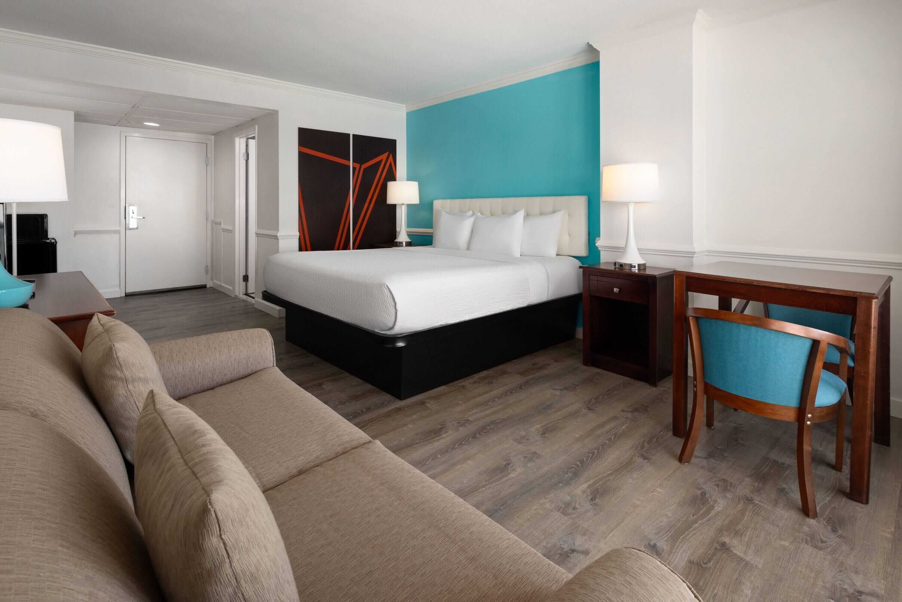 A hotel room with a bed, a desk, a chair, and a sofa.