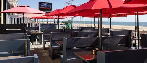 A deck with red umbrellas, seating, and a view of the beach.
