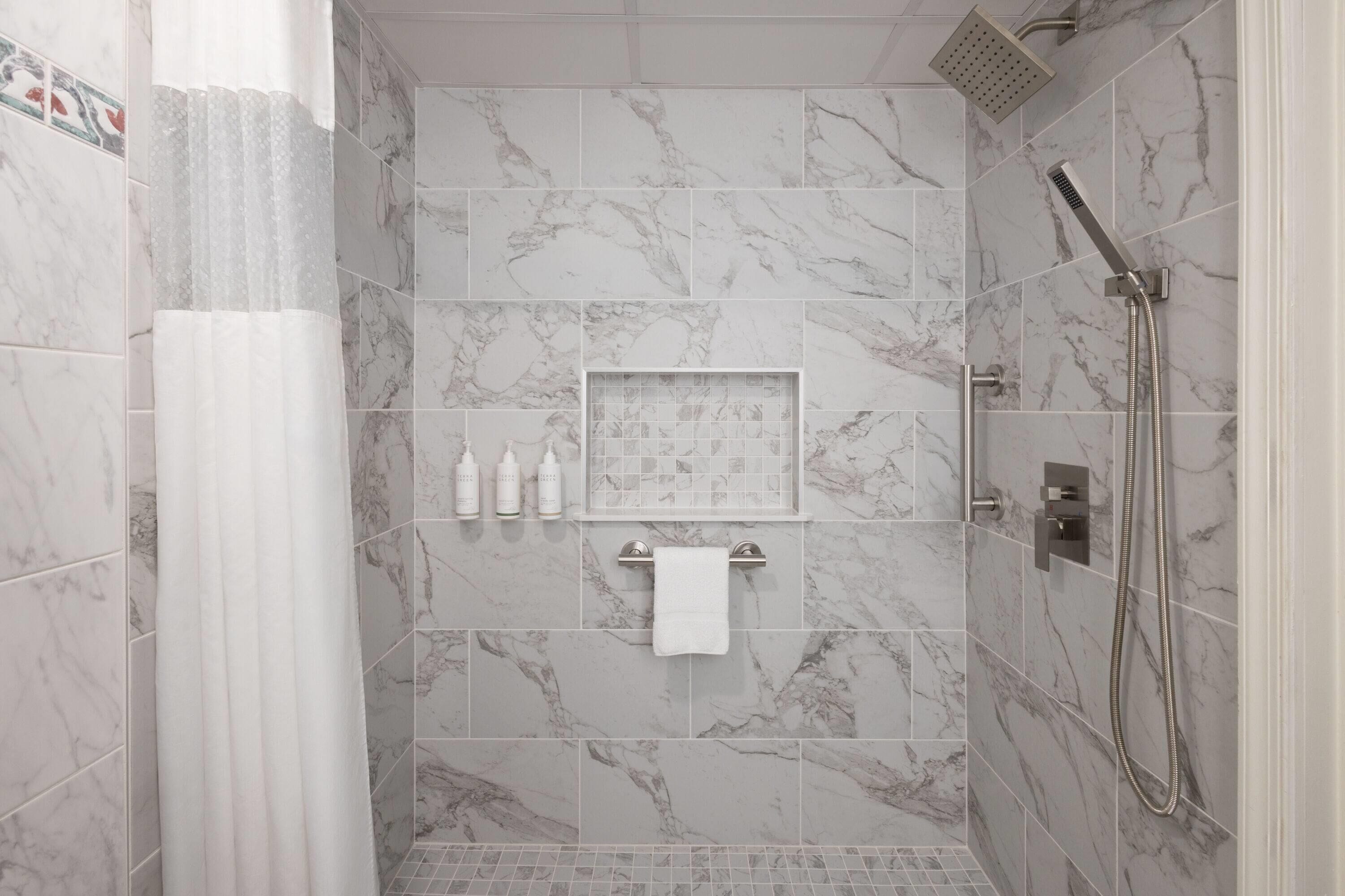 A walk-in shower with marble tiles, a handheld showerhead, and a towel rack with a white towel.