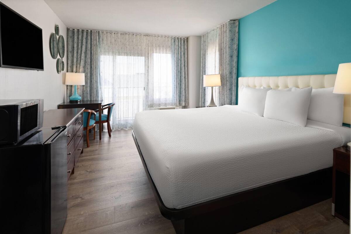 Une chambre d’hôtel avec un grand lit, un bureau avec une chaise, une télévision et un meuble pour la télévision.