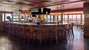 A bar area with a central island, multiple stools, and a variety of bottles and glasses.