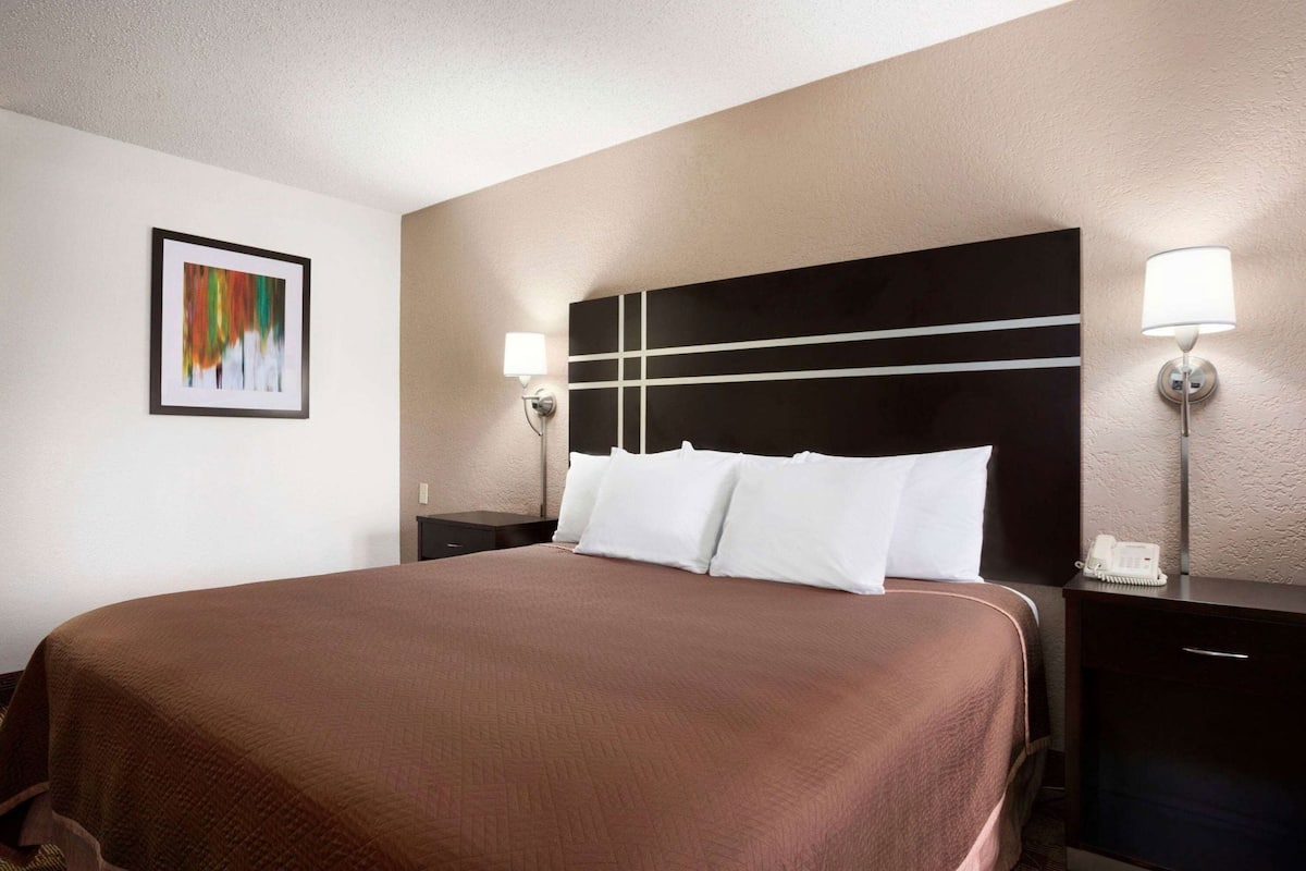 A hotel room with a large bed, two bedside tables, a headboard, a wall-mounted phone, and a framed picture on the wall.