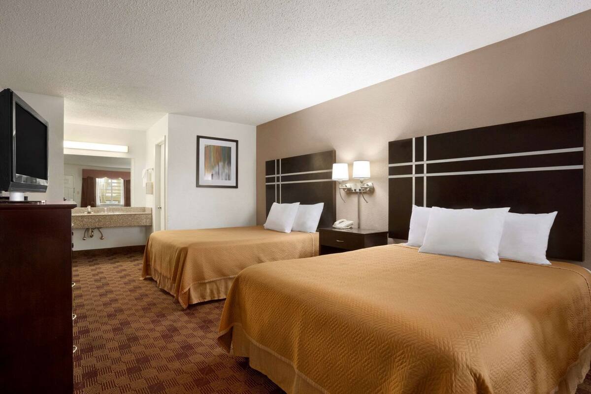 A hotel room with two beds, a TV, a desk, and a bathroom.