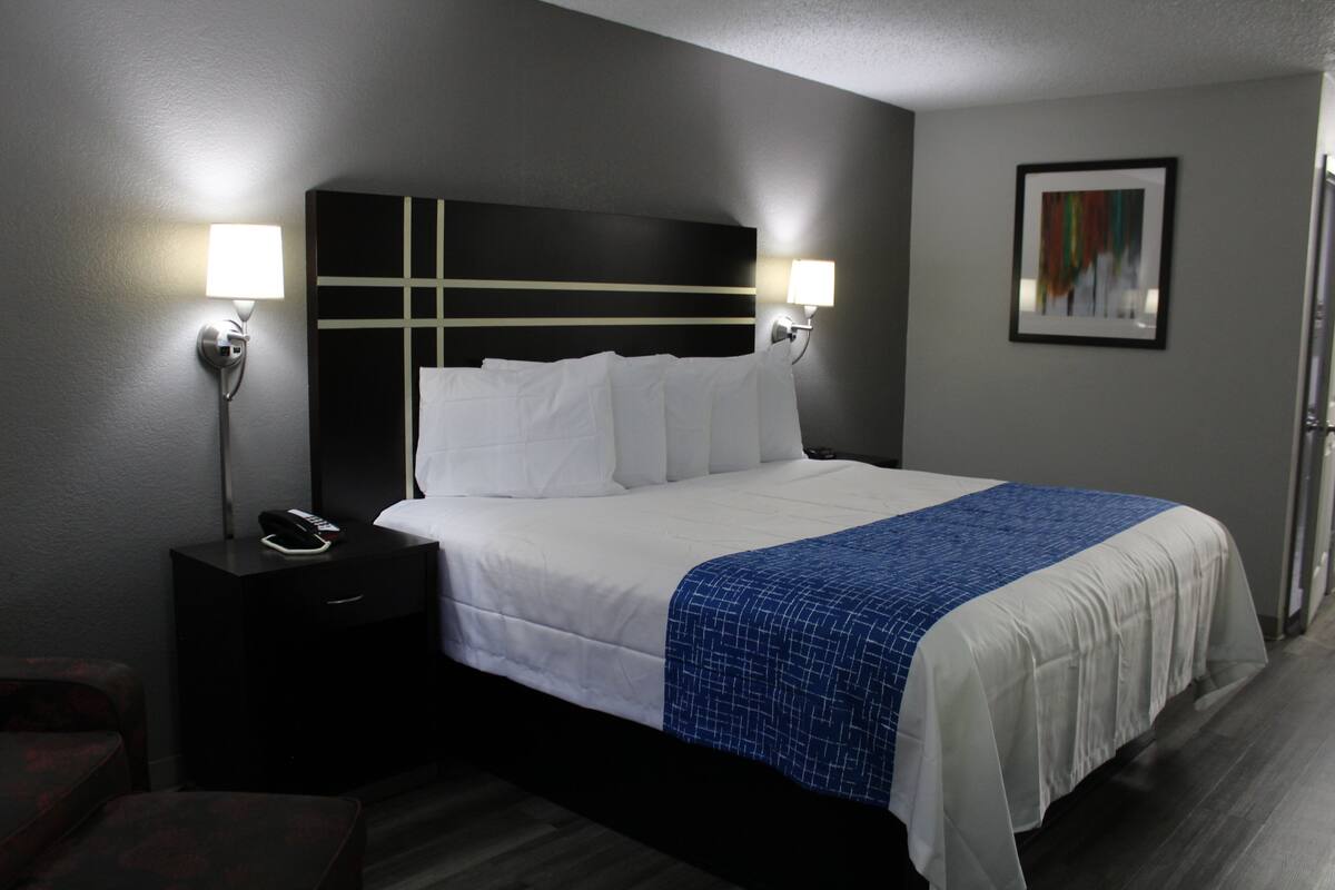 A hotel room with a large bed, two bedside lamps, a nightstand with a phone, and a framed picture on the wall.
