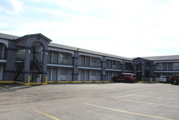A multi-story motel with a central staircase, parking lot, and several vehicles parked in front.