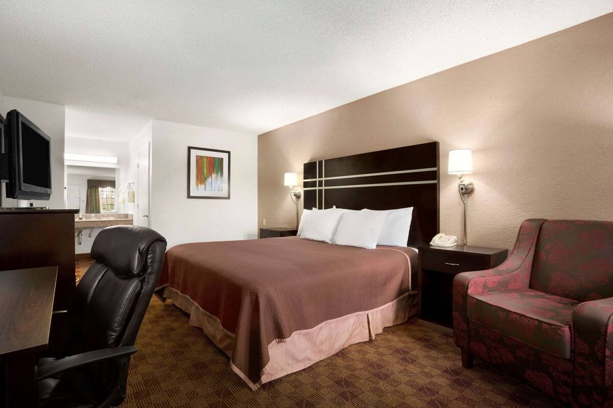 A hotel room with a bed, a desk, a chair, a television, and a painting on the wall.