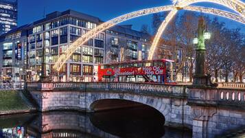 Ein roter, zweistöckiger Bus mit der Aufschrift 'Visit Düsseldorf Hop On Hop Off', eine Brücke und ein Spiegelteich.