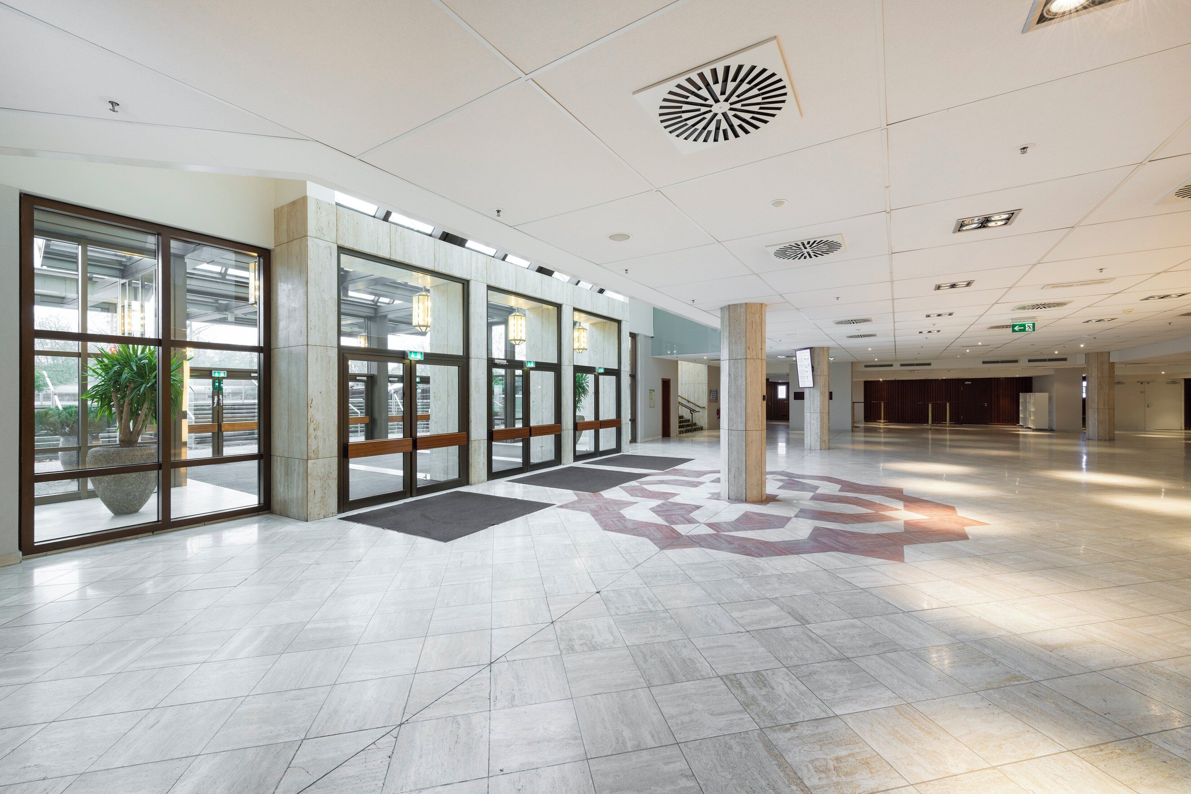 Un hall d’entrée spacieux avec un sol en marbre, de grandes portes vitrées et un design de plafond moderne.