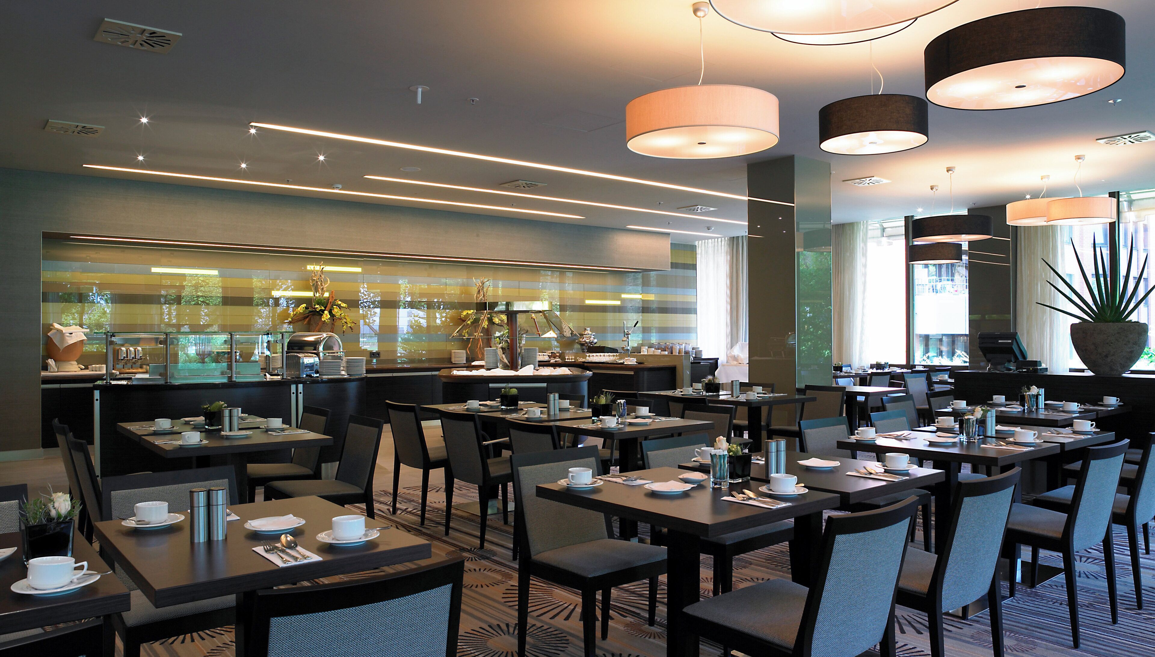 Ein modernes Restaurant mit mehreren Tischen, Stühlen, einer sichtbaren Küche und Pendelleuchten.