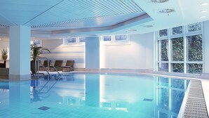 Una piscina interior con agua cristalina, sillas de descanso y un amplio ventanal que proporciona luz natural.