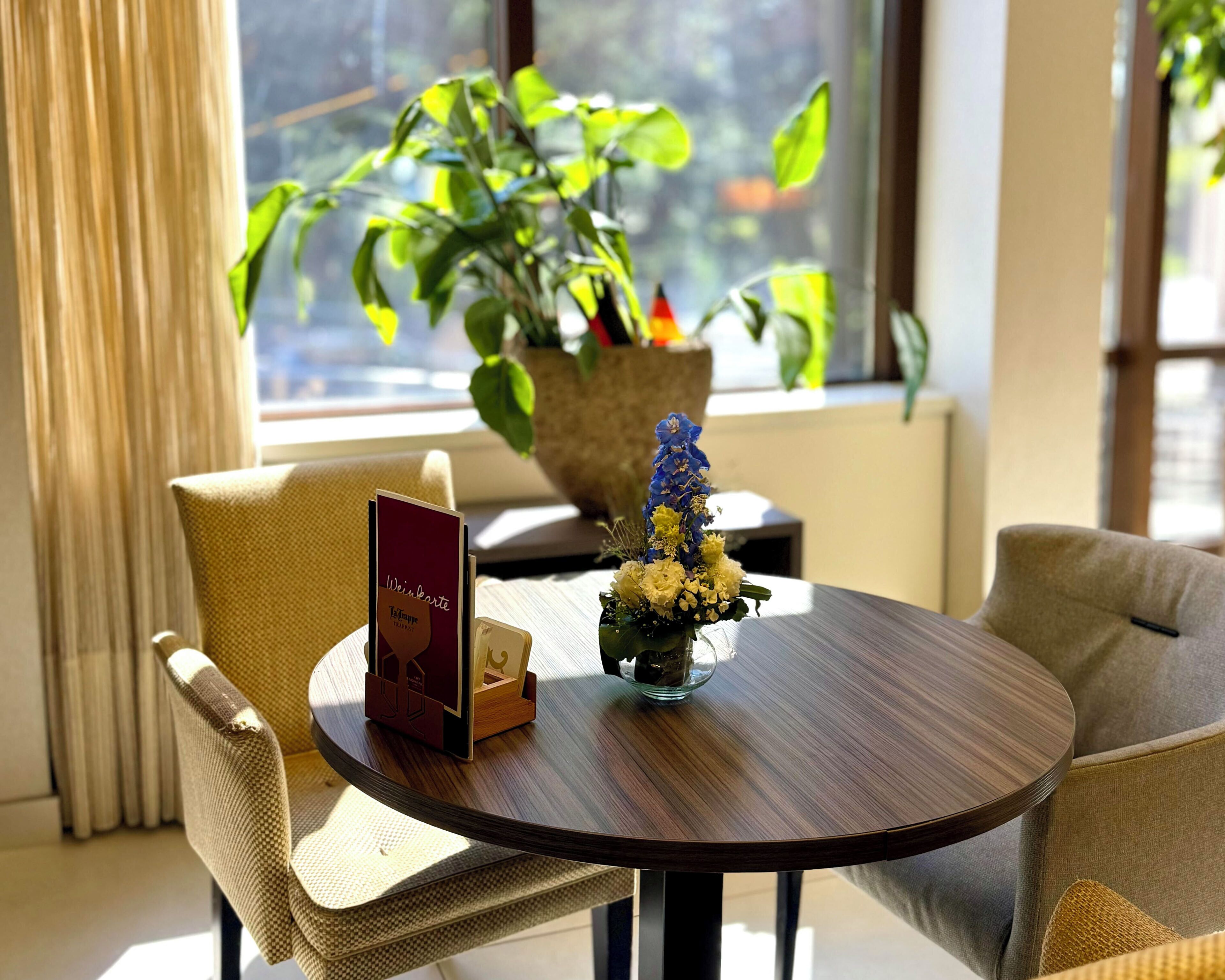 A round wooden table with a vase of flowers, a menu, and a small card stand.