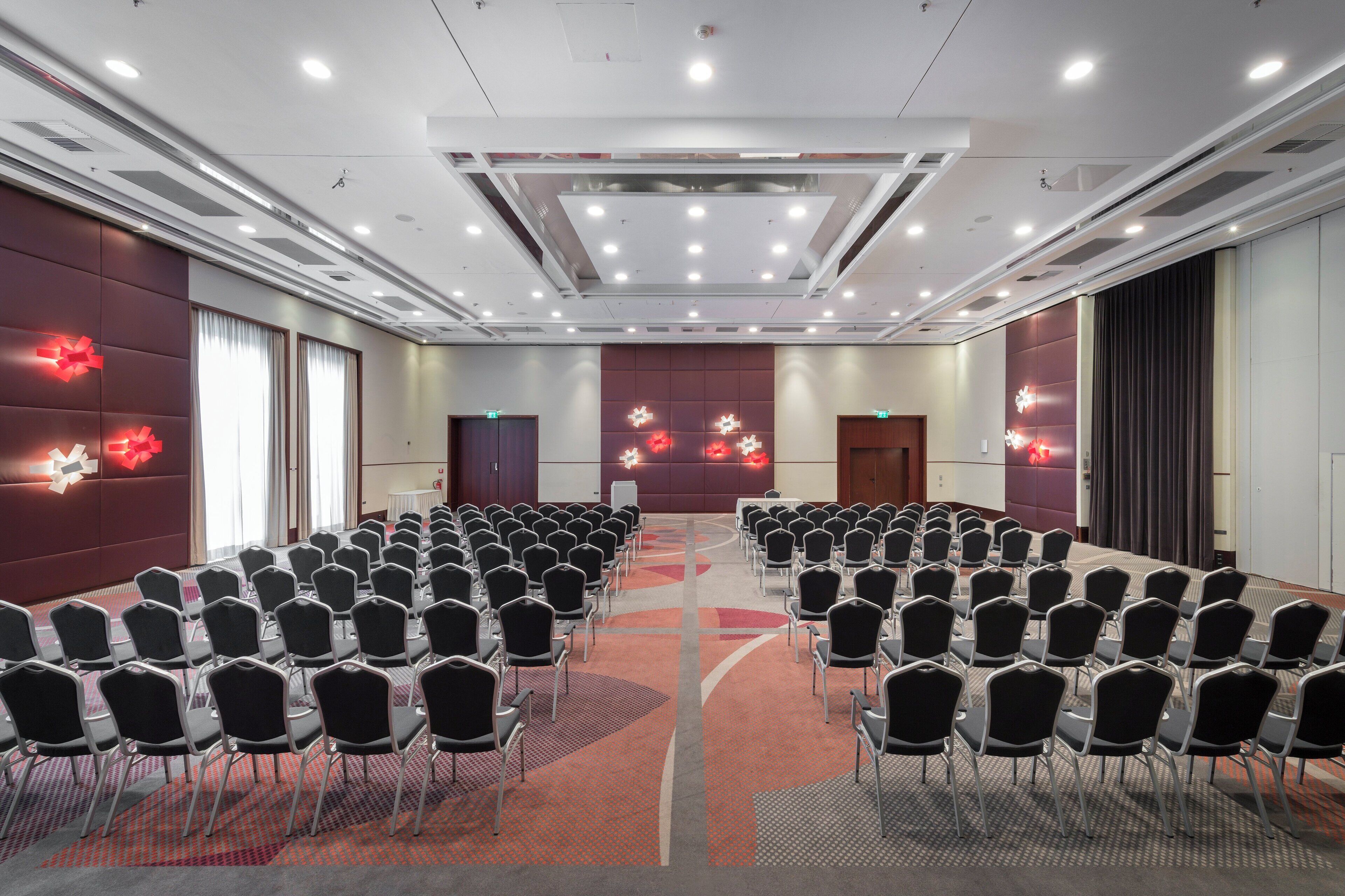 Une salle de conférence avec des rangées de chaises, une scène et un grand écran.