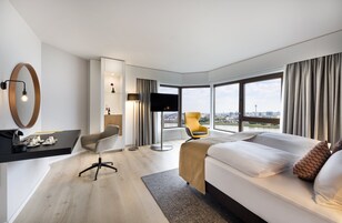 Una habitación de hotel moderna con una cama grande, un escritorio, una silla y vistas a la ciudad.