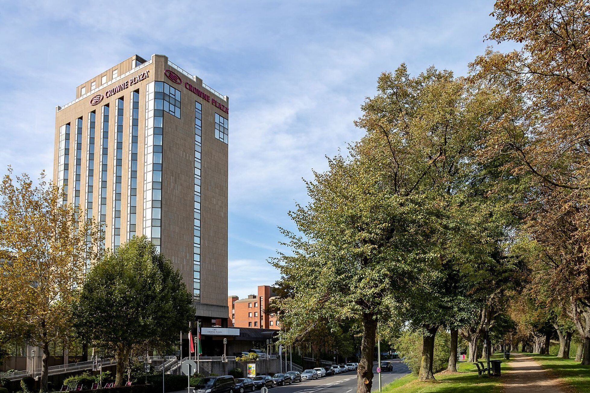 Un edificio de hotel de diseño moderno, un área de estacionamiento y una calle arbolada.