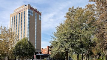 Un edificio de hotel de diseño moderno, un área de estacionamiento y una calle arbolada.