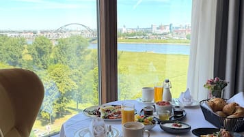 A dining table with breakfast items and a view of a bridge and cityscape.