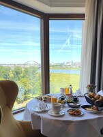 Una mesa de comedor con alimentos para el desayuno y vista a un puente y un paisaje urbano.