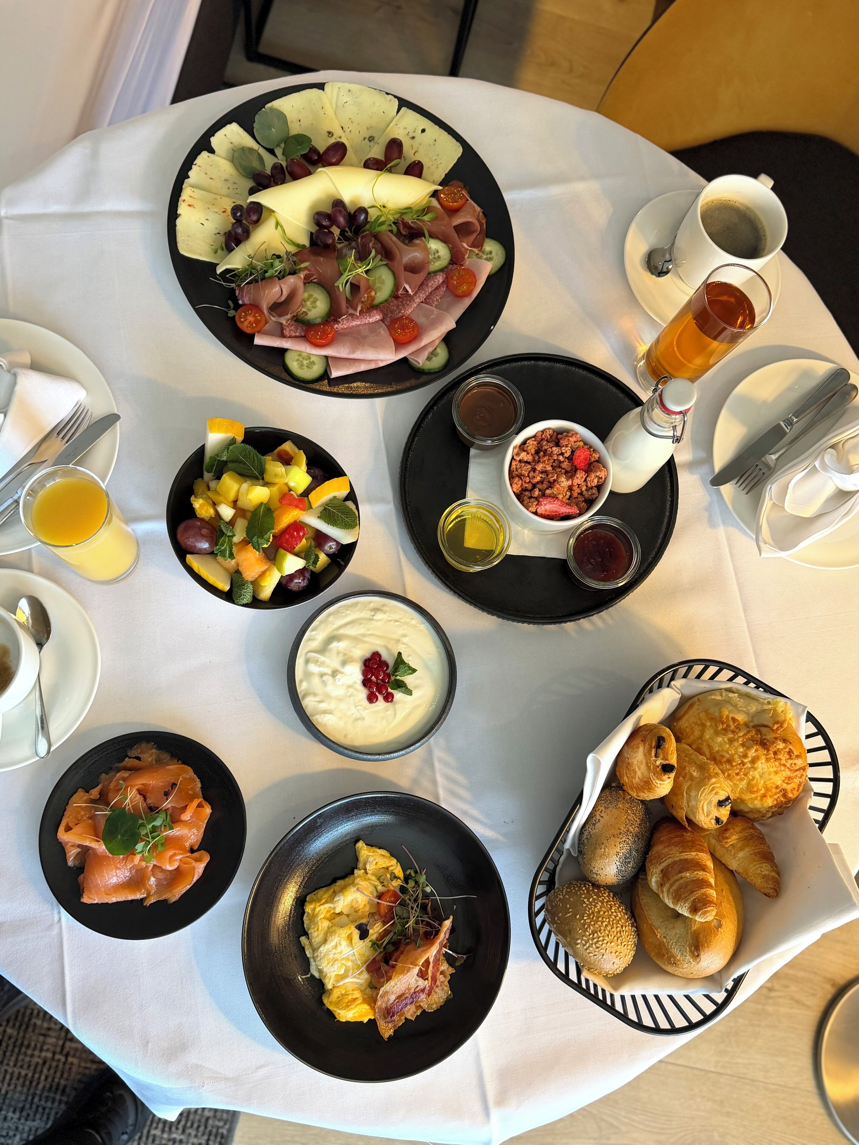 Ein Tisch ist reichhaltig mit verschiedenen Speisen gedeckt, darunter ein Obstsalat, eine Käseplatte und Gebäck.
