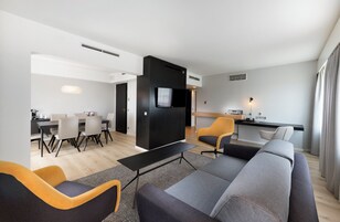 Un salon moderne comprenant un canapé, des fauteuils, un coin repas avec une table et des chaises, et une petite cuisine équipée d’un téléviseur et d’une petite table.