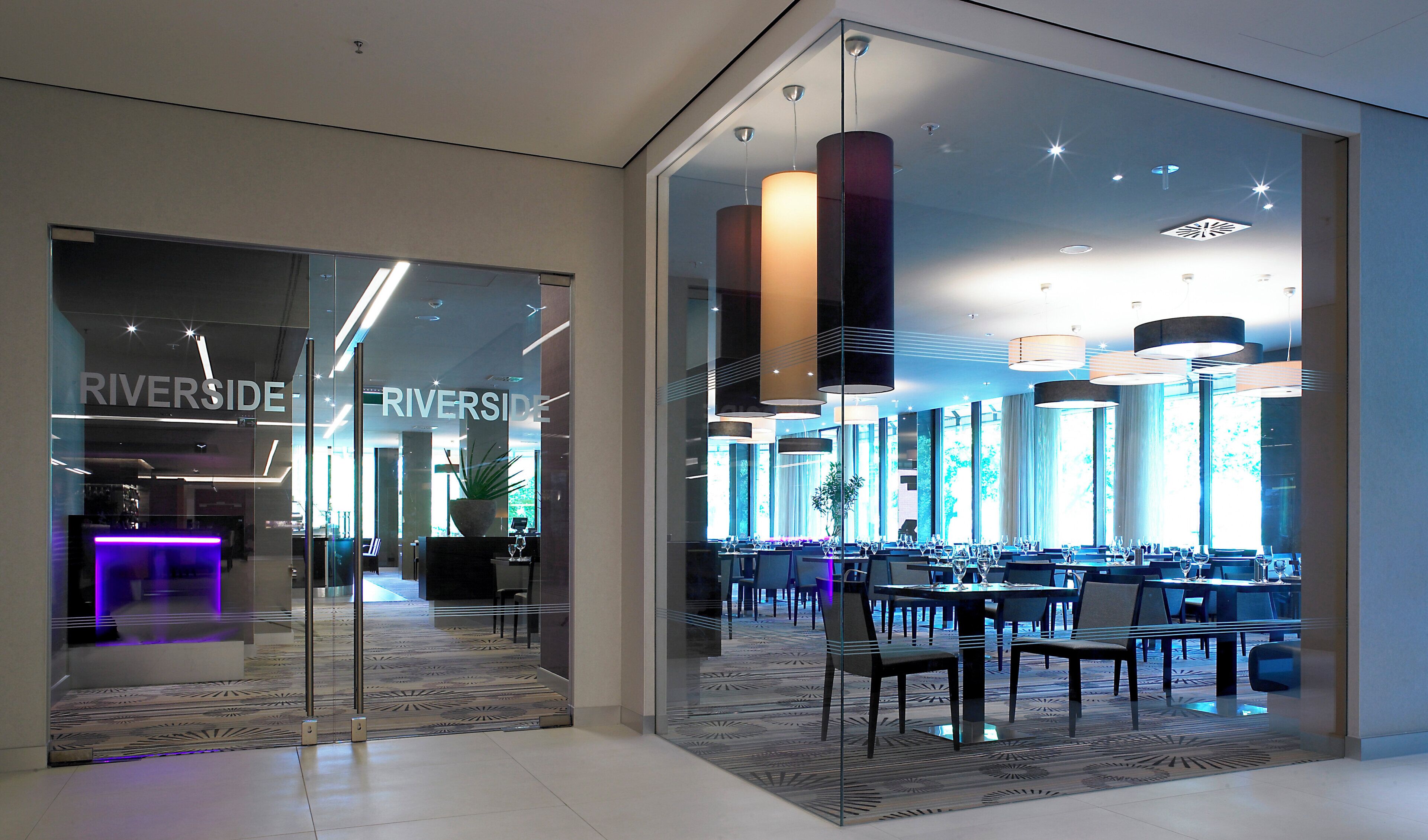 Eine moderne Hotelhalle mit Glastür, einer Rezeption und einem Essbereich mit Tischen und Stühlen.