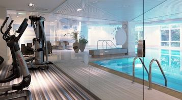A gym with exercise equipment and a glass wall leading to a swimming pool.