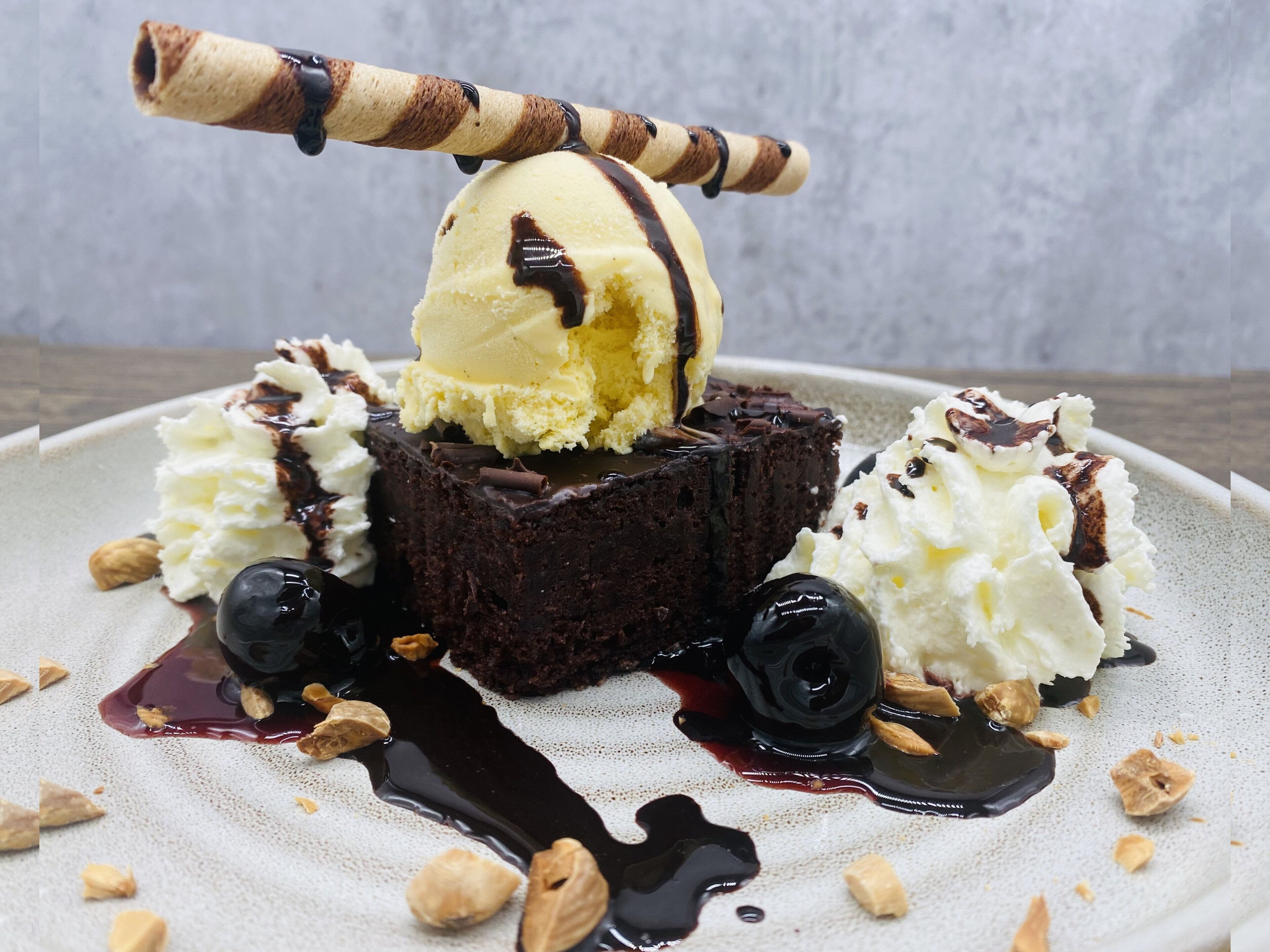 Sobremesa com uma bola de sorvete sobre um bolo de chocolate, acompanhada de chantilly e calda de chocolate.
