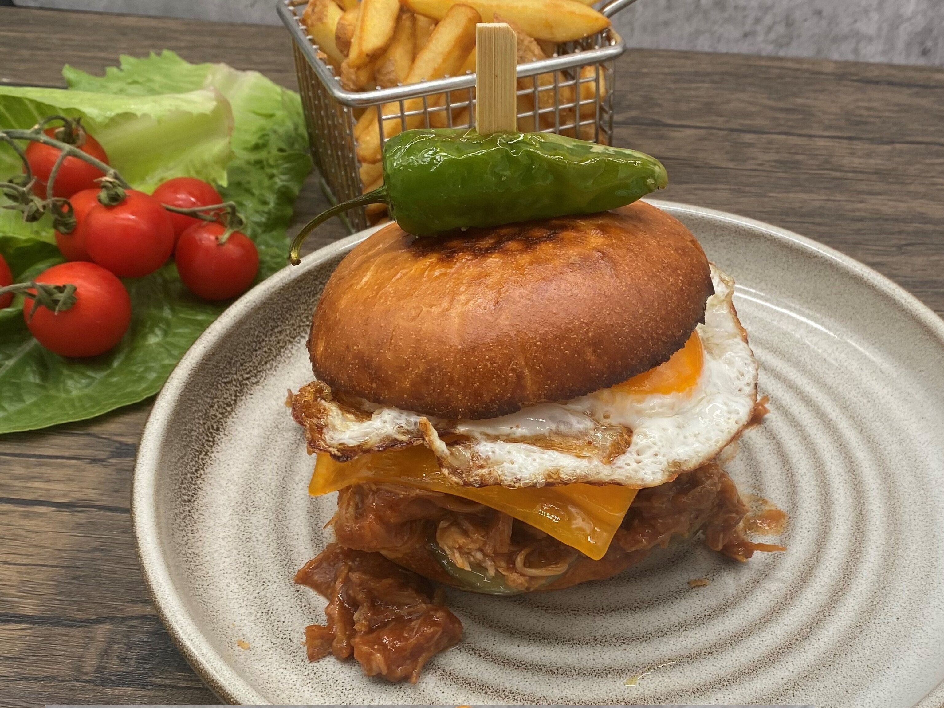 Ein Sandwich mit Spiegelei und grüner Chili, serviert auf einem Teller mit Pommes und frischen Tomaten.