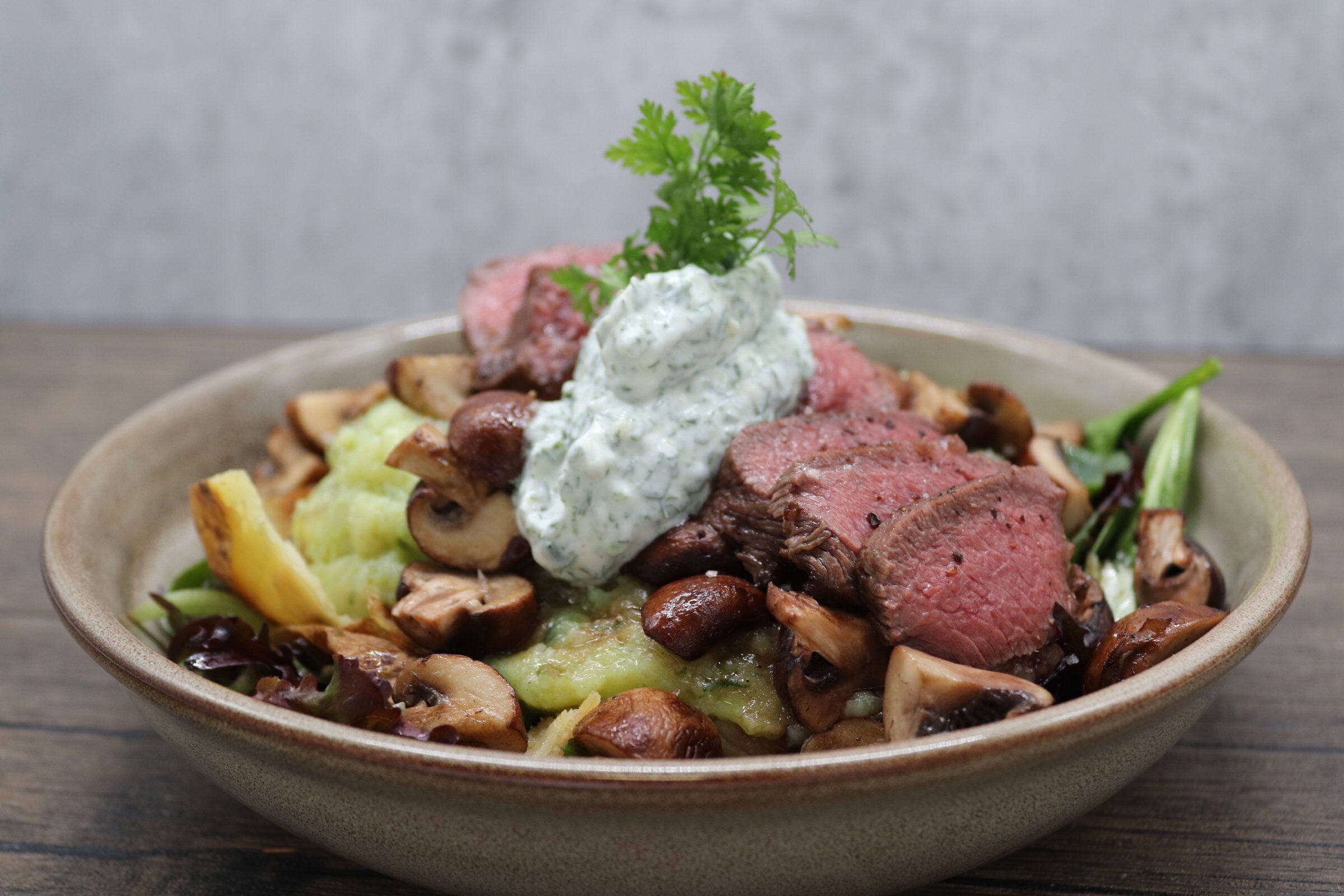 A bowl of food with meat, mushrooms, and a creamy sauce, garnished with parsley.