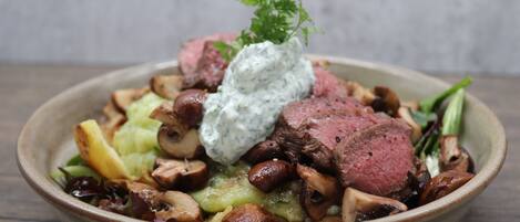 A bowl of food with meat, mushrooms, and a creamy sauce, garnished with parsley.
