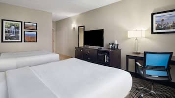 A hotel room with two beds, a desk with a computer, a chair, a TV, and framed pictures on the wall.