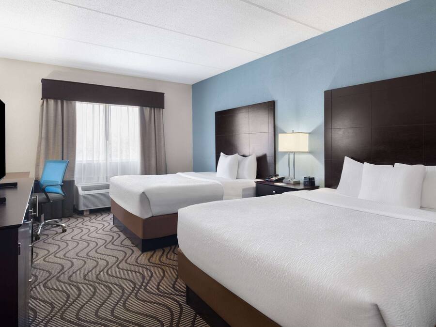 A hotel room with two beds, a desk, a chair, a TV, and a window with curtains.