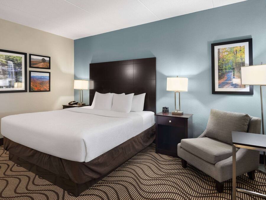 A hotel room with a large bed, a chair, two nightstands with lamps, and framed pictures on the walls.