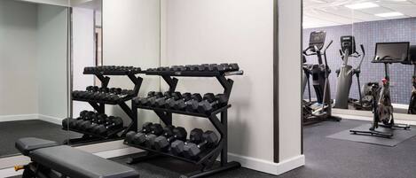 Un gimnasio con estantes para pesas, mancuernas, una banca y máquinas de cardio.