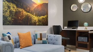 Una sala de estar moderna con un cuadro de paisaje amplio, un sofá cómodo con cojines estampados, un escritorio con una computadora portátil e impresora.
