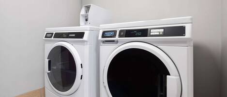 Two front-loading washing machines in a laundry room with a wooden floor and white walls.
