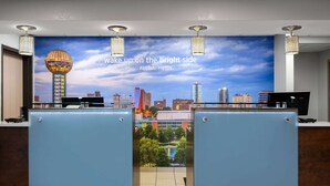 Ein Hotel-Empfangsbereich mit Stadtbild-Wandgemälde, einer Rezeption und Blick auf Pool und Gebäude.