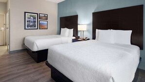 Ein Hotelzimmer mit zwei Betten, einem Nachttisch mit Lampe und gerahmten Bildern an der Wand.