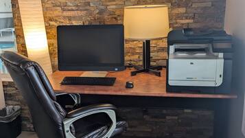 Escritorio de madera con monitor de computadora, teclado e impresora. Una silla de cuero negro está ubicada frente al escritorio.