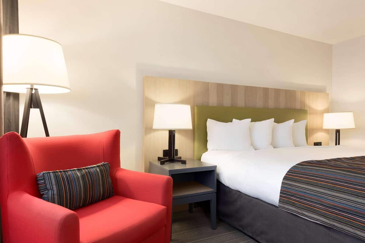 Habitación de hotel con una cama, un sillón rojo, dos mesitas de noche con lámparas y un cabecero con diseño de panel de madera.