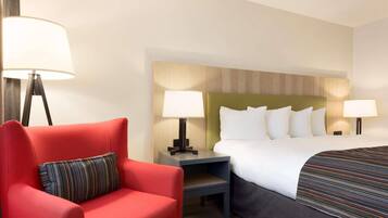 A hotel room with a bed, a red armchair, two bedside tables with lamps, and a headboard with a wooden panel design.