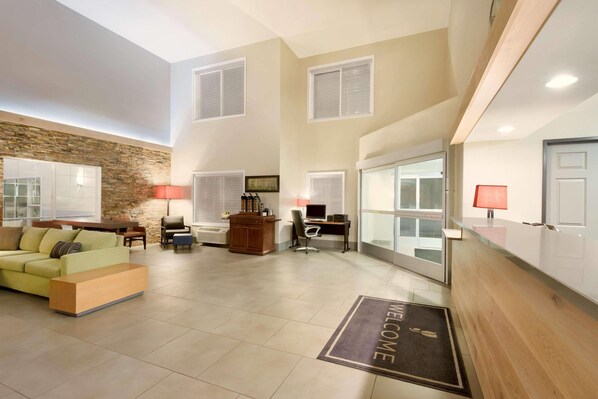 A spacious living area with a sofa, a coffee table, a desk with a computer, and a fireplace. There is a welcome mat at the entrance.