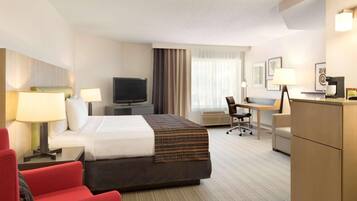 Een hotelkamer met een bed, bureau, stoel, televisie en een rode fauteuil.