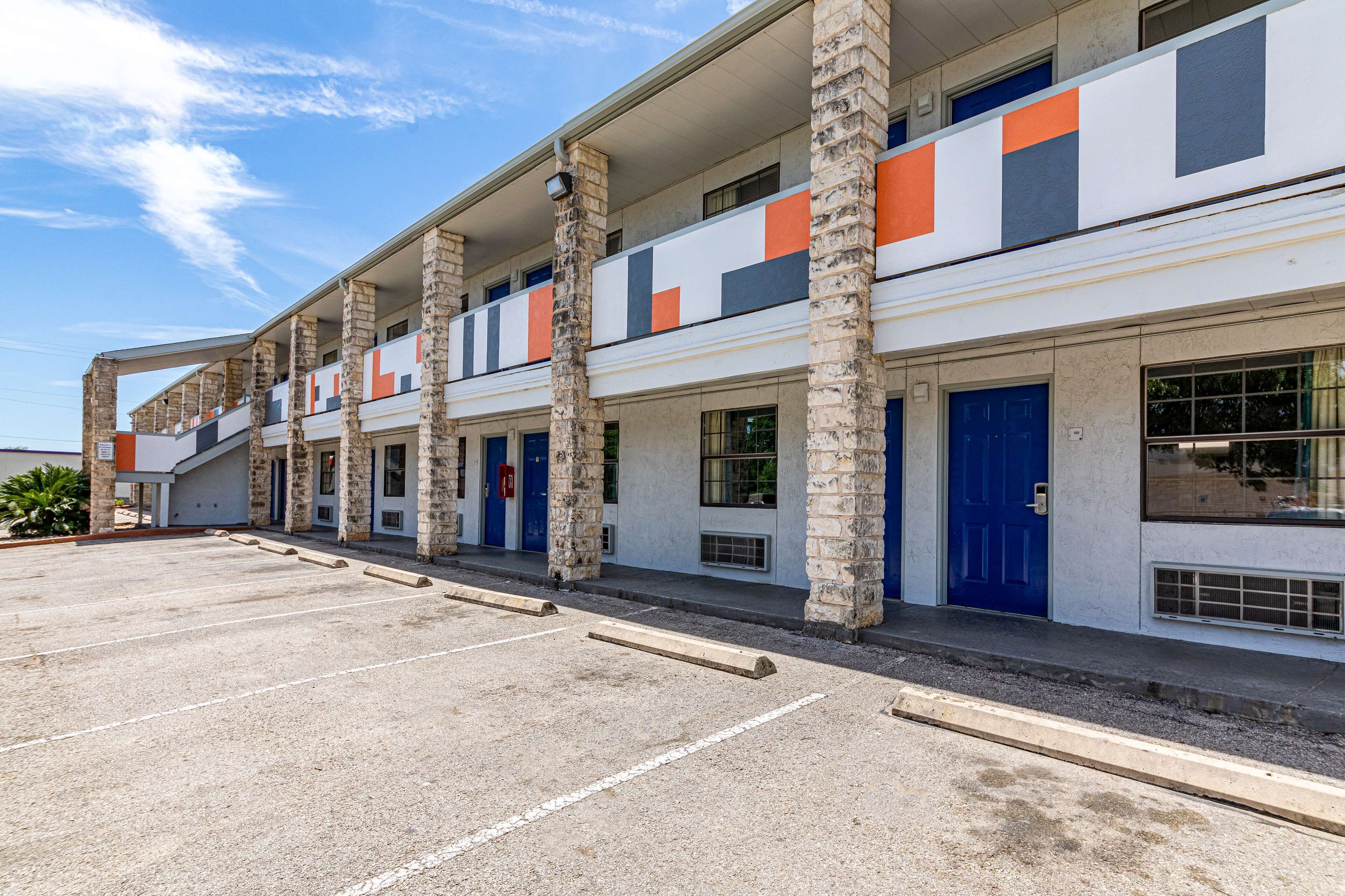 Un hôtel à plusieurs étages, avec une rangée de chambres, chacune dotée d’une porte bleue et de fenêtres.